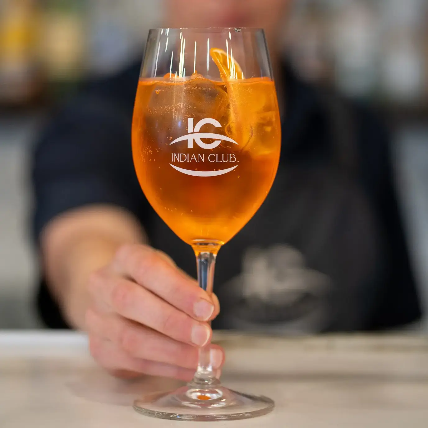 Server presenting a semi-transparent orange-coloured drink.