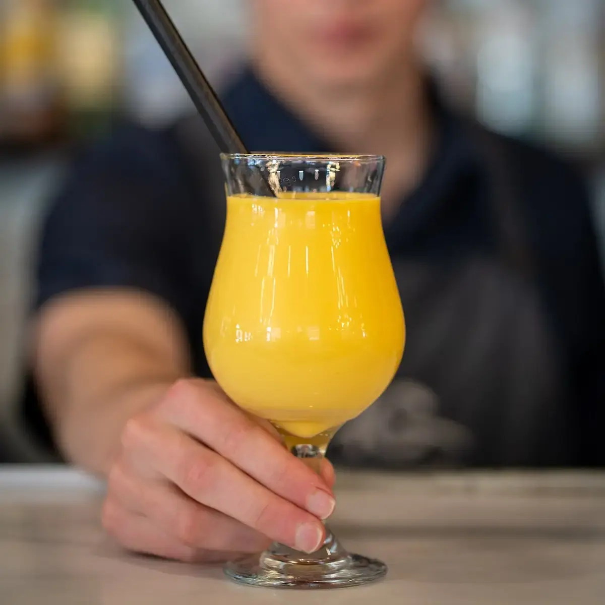 Server presenting an opaque yellow-orange-coloured drink.