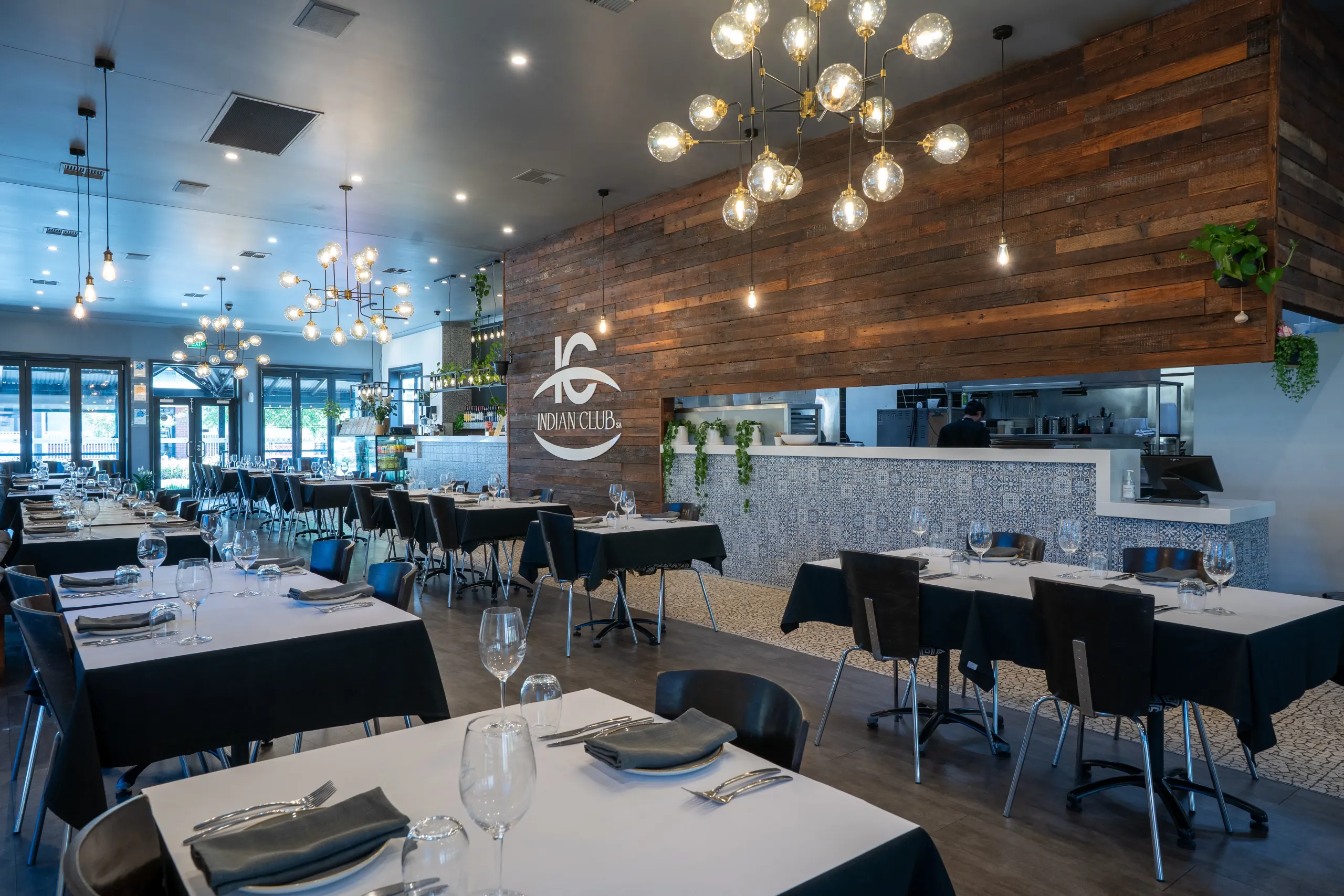Interior of Indian Club SA restaurant with tables, the logo on a wall, and lights.